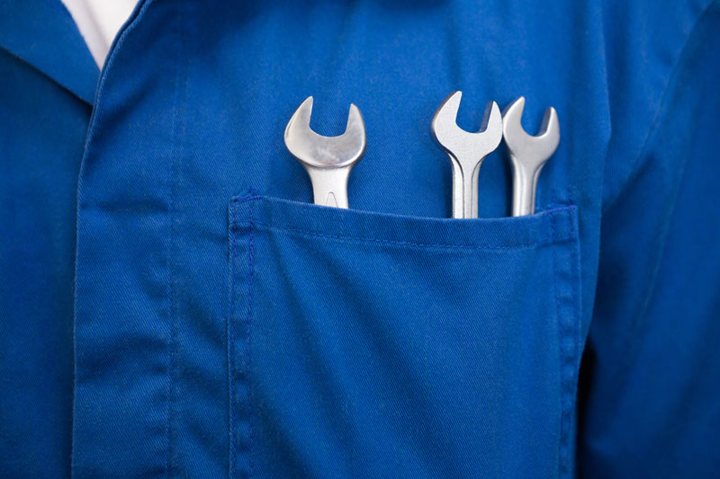 Three small wrenches in front chest pocket of mechanic wearing blue jumpsuit